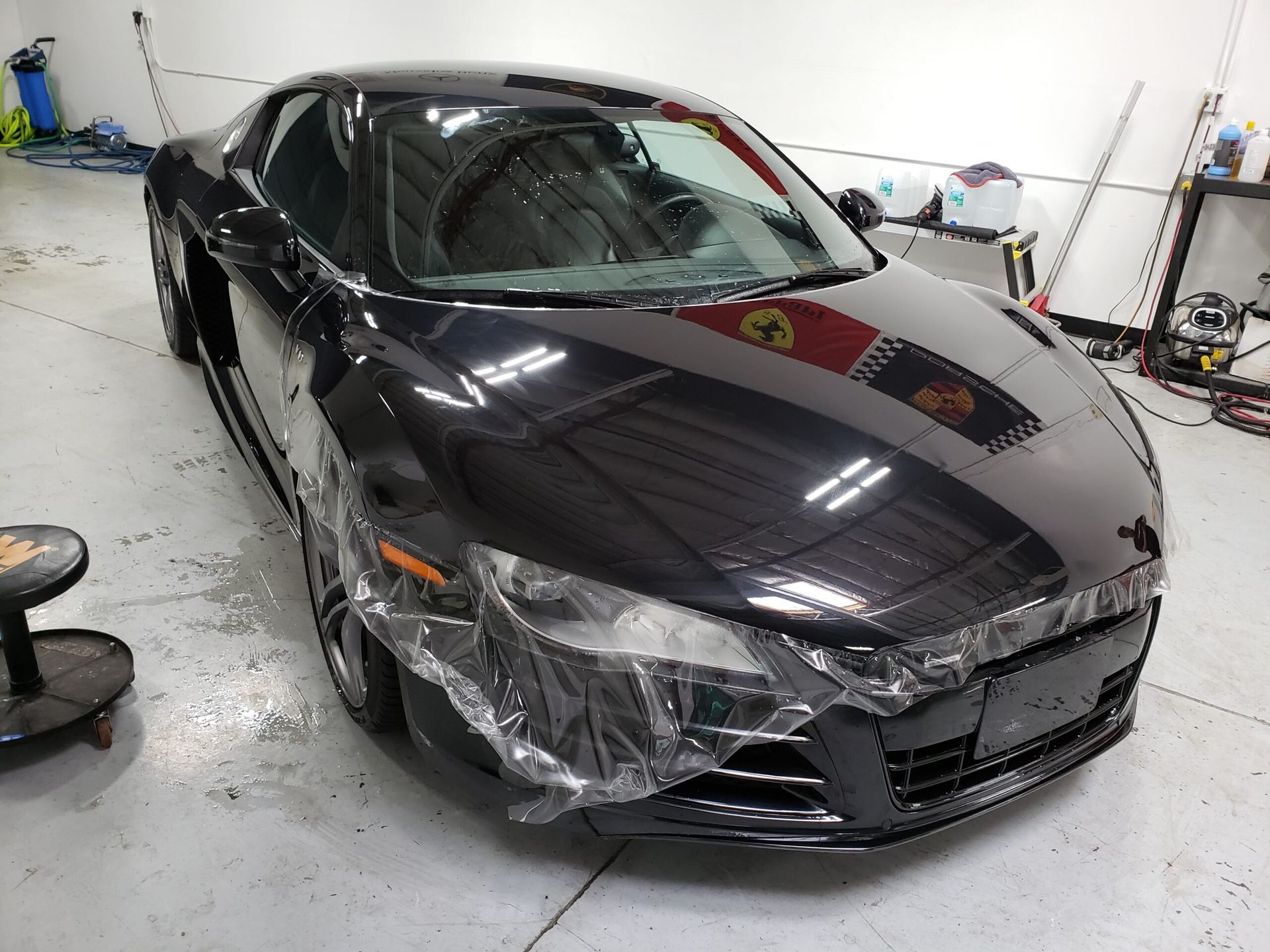 Black sedan with damaged front end in a garage, bumper and headlights covered in plastic wrap