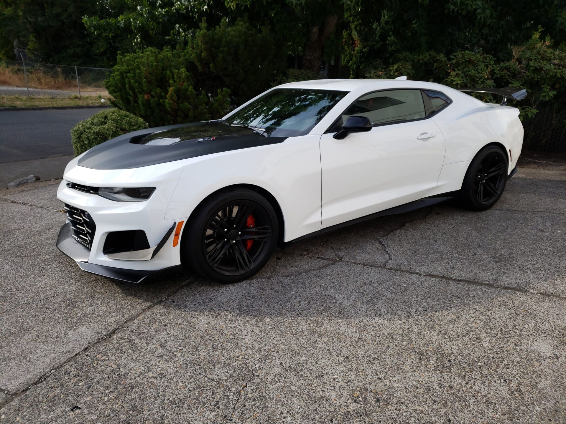 White sports coupe parked on a gravel lot, with black wheels and red brake calipers