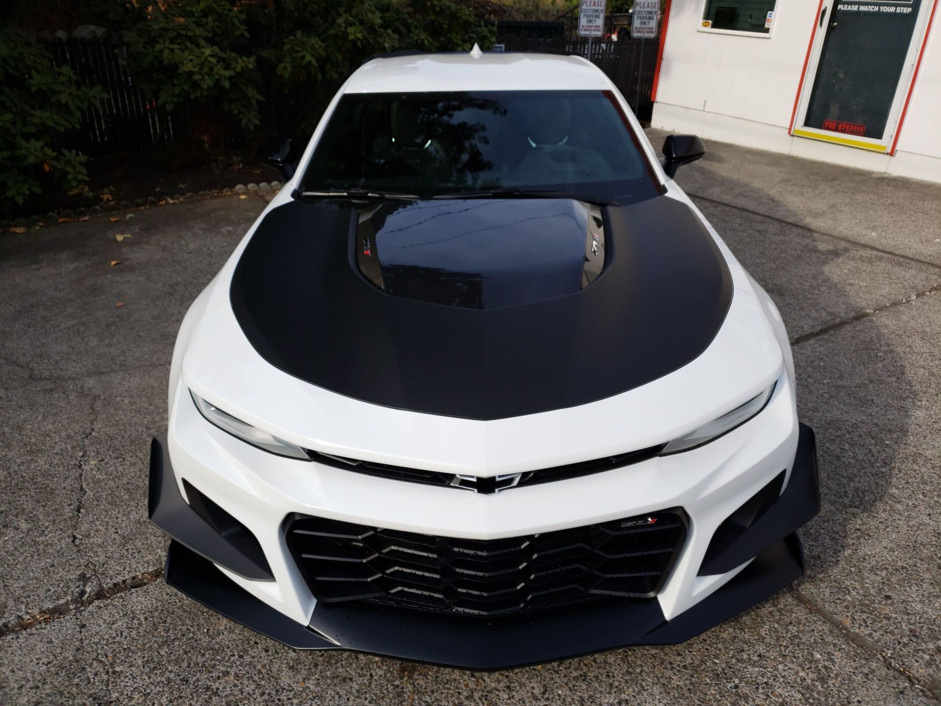 White sports car with black hood parked outdoors, front view