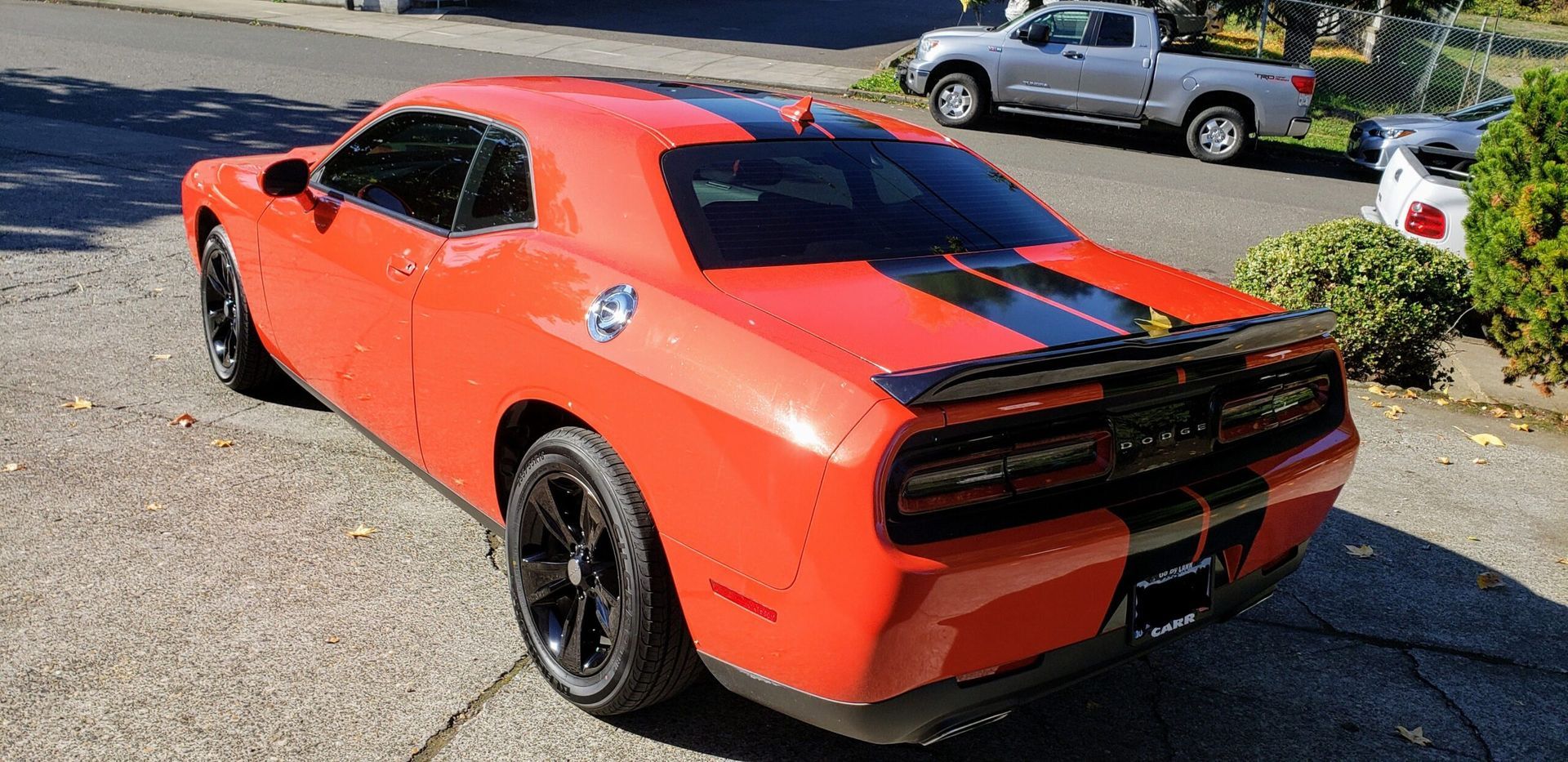 Orange sports car with black racing stripes parked outdoors on pavement