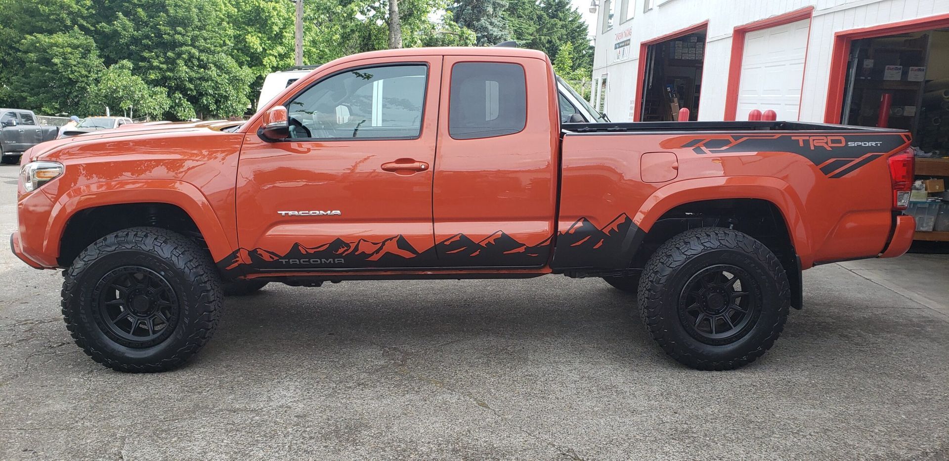 Orange lifted pickup truck with black wheels parked on a gravel surface
