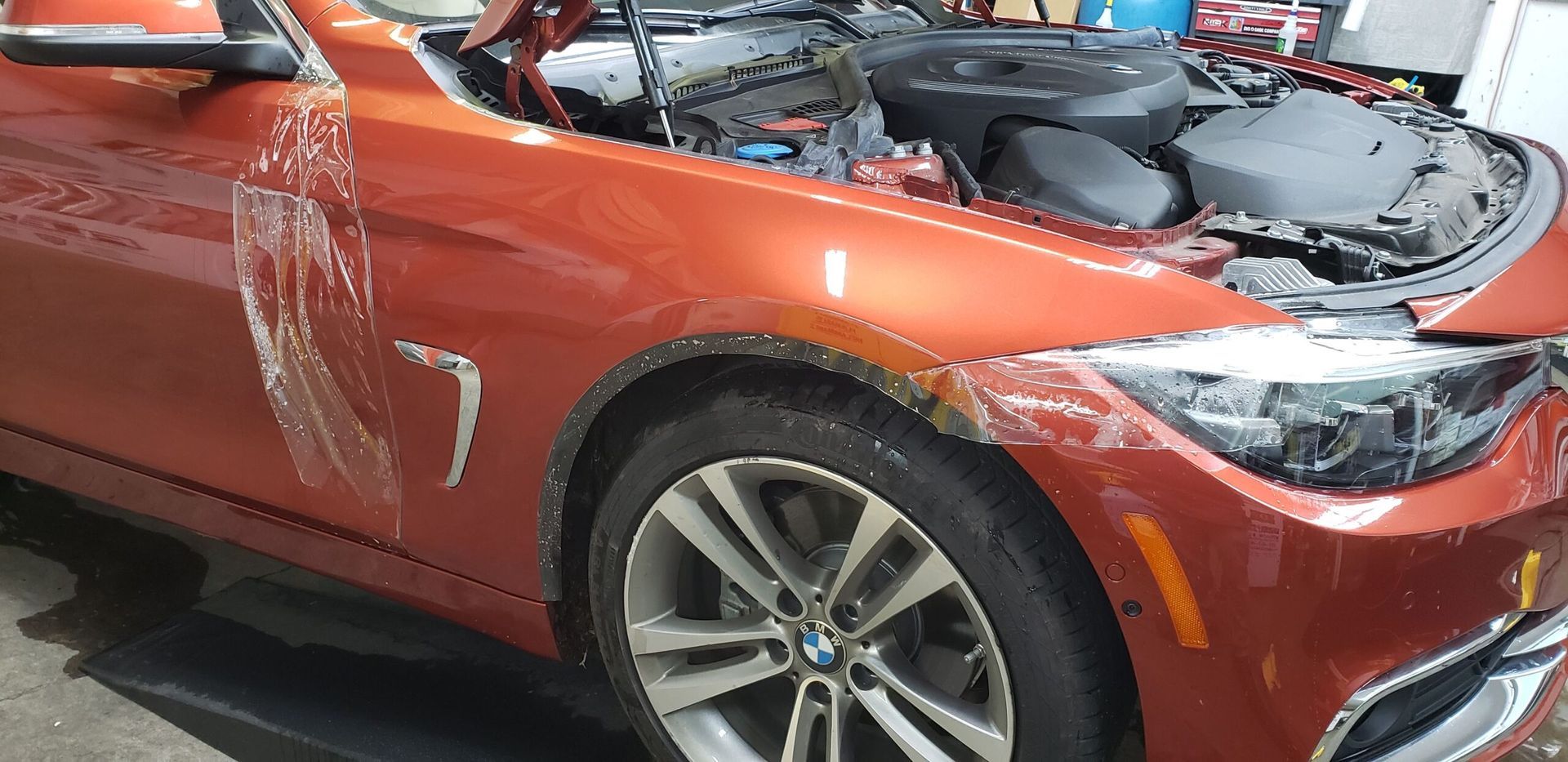 Orange car with front-end damage and hood open in a garage