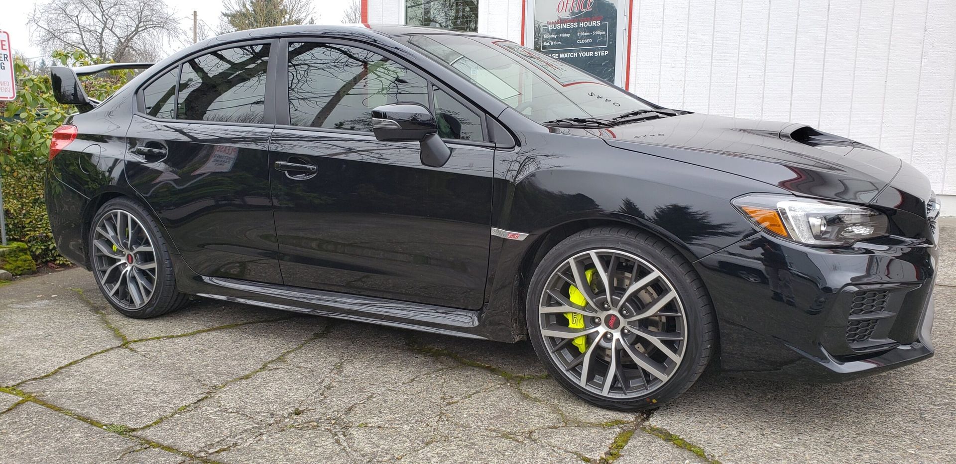 Black sedan parked beside a white wall, showing bright yellow brake calipers and silver alloy wheels.