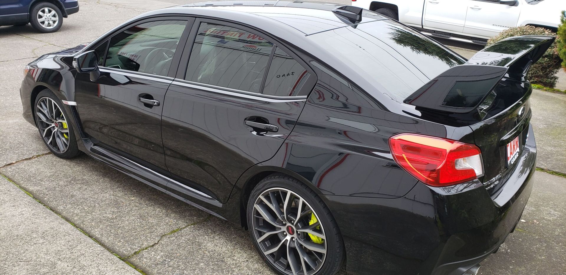 Black sports sedan parked outdoors, side view with tinted windows and a rear spoiler.