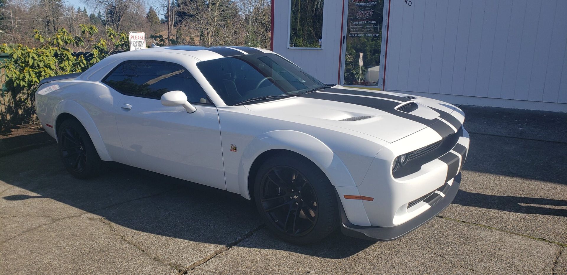 White sports car with black wheels parked outdoors in sunlight