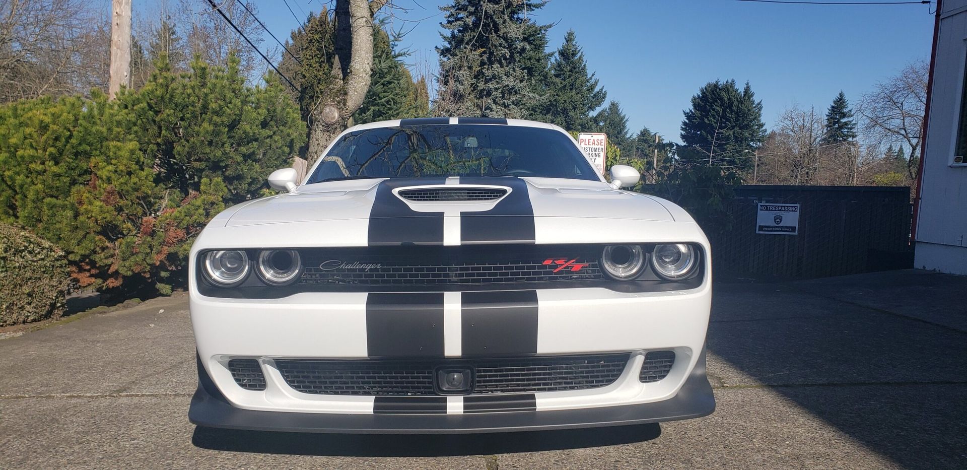 Front view of a white sports car with black racing stripes parked on a driveway in sunlight