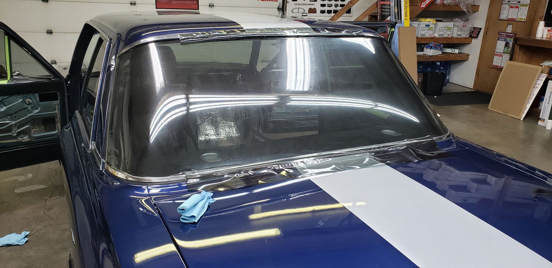 Blue car indoors with a wide white racing stripe and large windshield in a garage or workshop