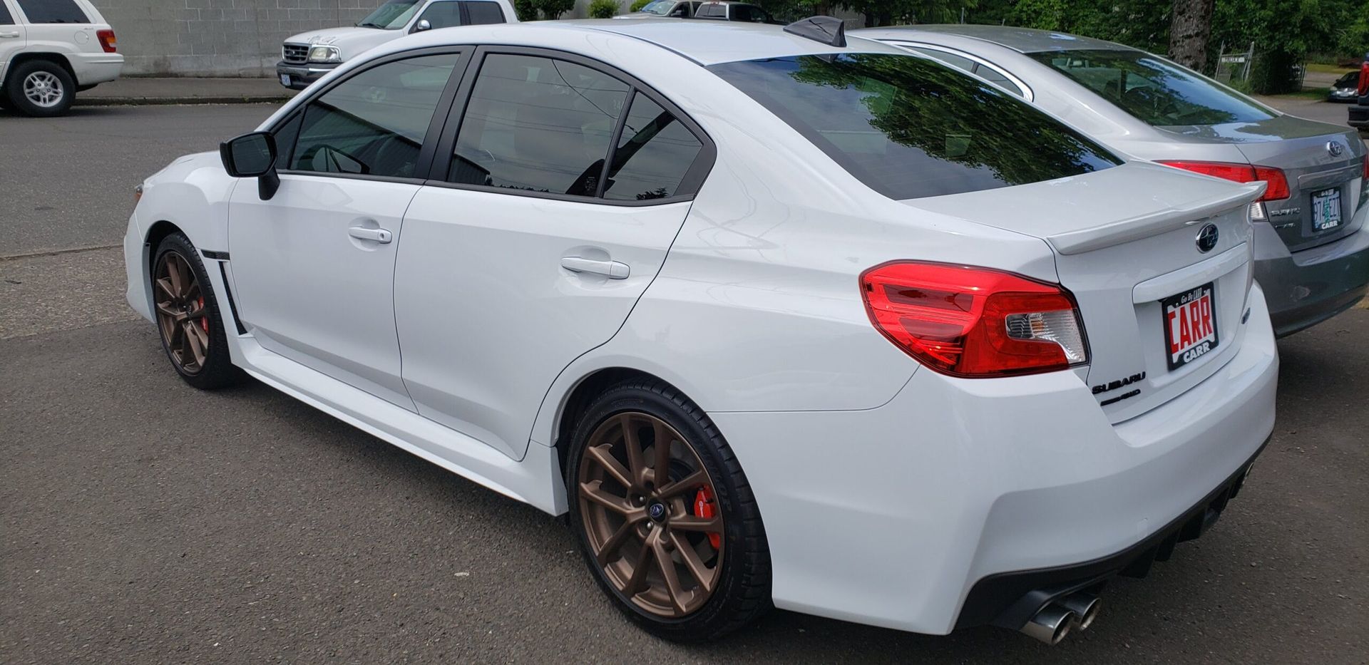 White sports sedan parked outdoors, rear three-quarter view, with bronze rims and tinted windows