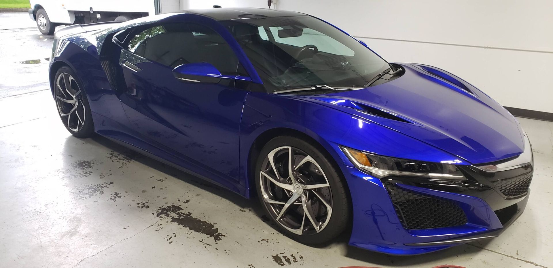 Blue sports car parked indoors on a wet floor, shown from the front-left side.