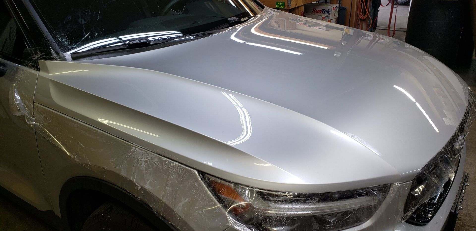 Silver car hood and front grille seen from above in a garage or workshop.