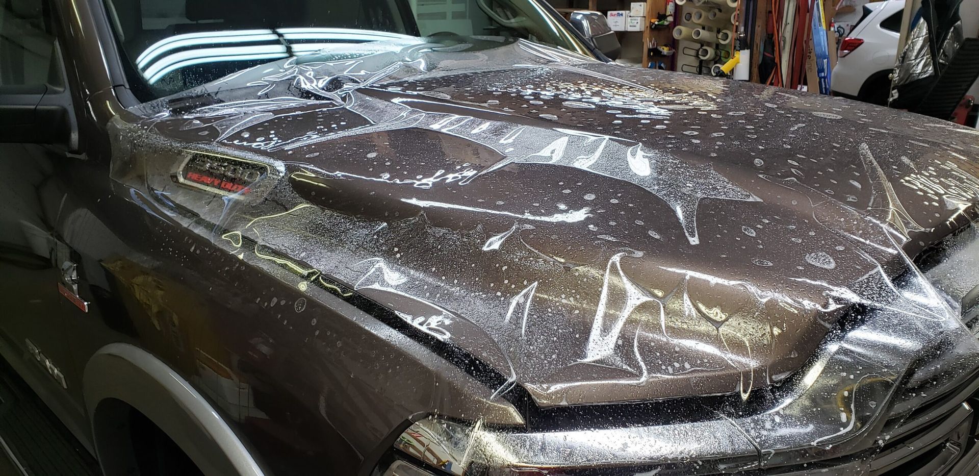 Crushed car front covered in shattered glass and a clear plastic sheet in a garage.