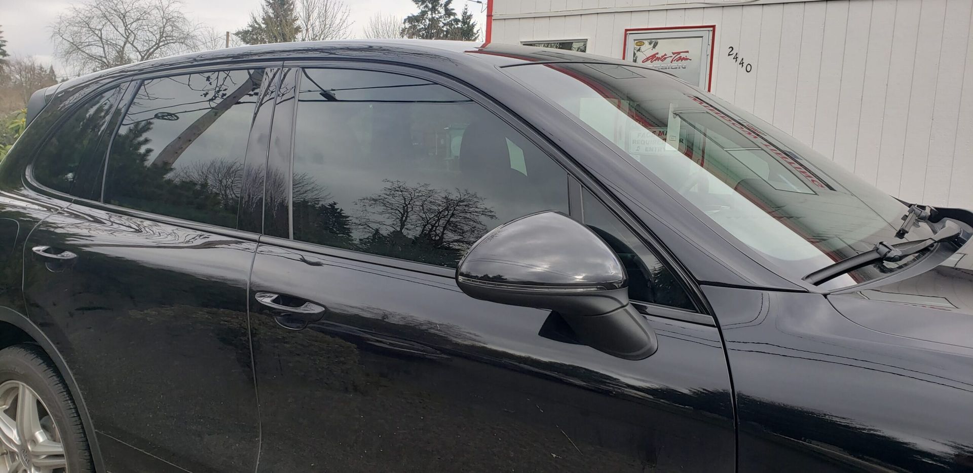 Black sedan parked beside a fence, seen from the side.