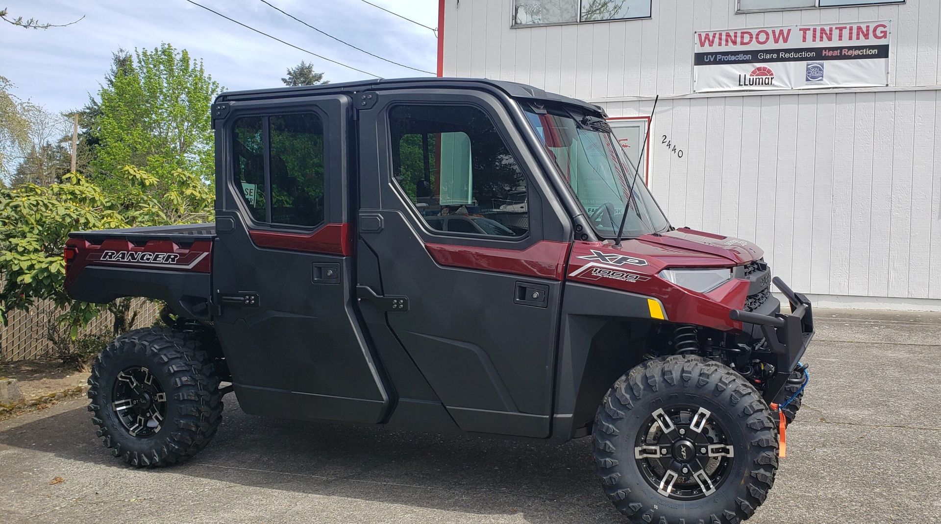 Black and red side-by-side utility vehicle parked beside a building with a “Window Tinting” sign
