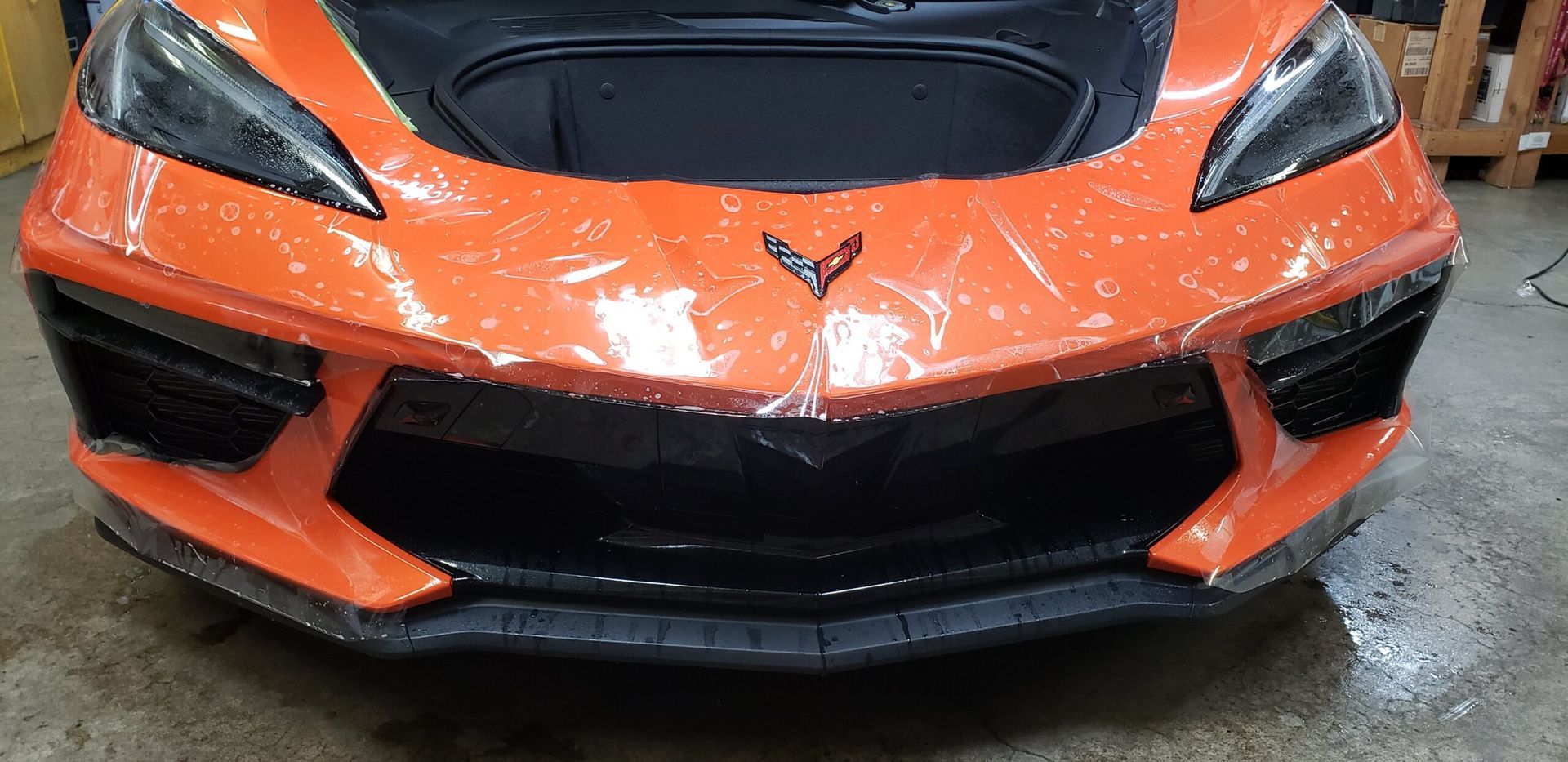 Front view of an orange sports car with a black hood, damaged bumper, and visible front-end damage.