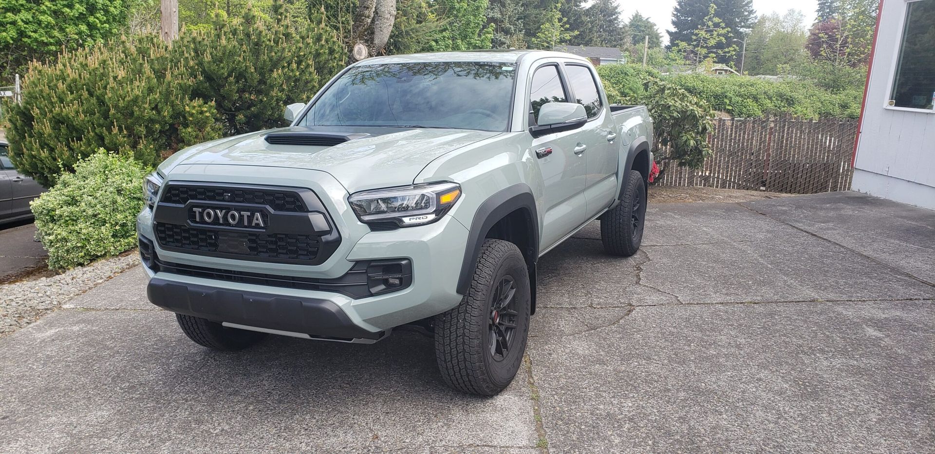 Light gray Toyota pickup truck parked on a driveway beside a house and garden greenery