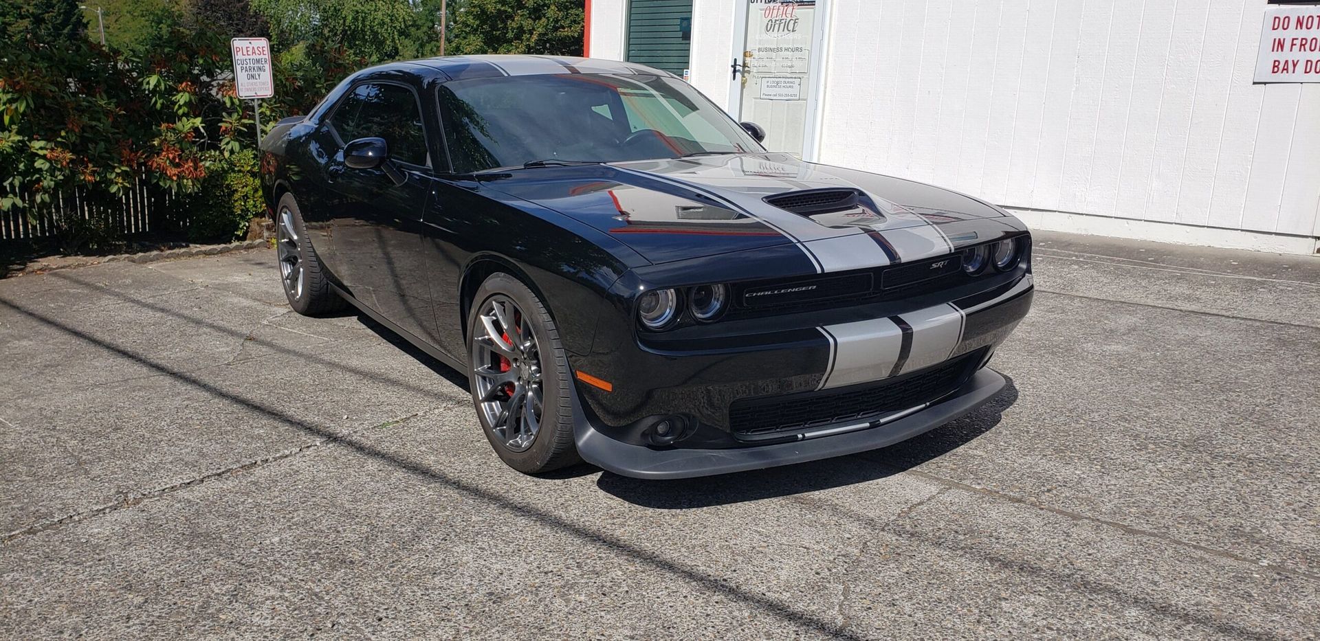 Black sports car parked outdoors in sunlight, front three-quarter view.