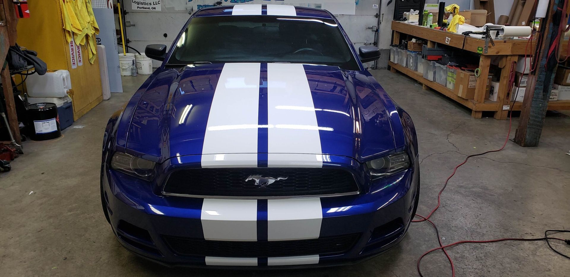 Blue Ford Mustang with white racing stripes in a garage