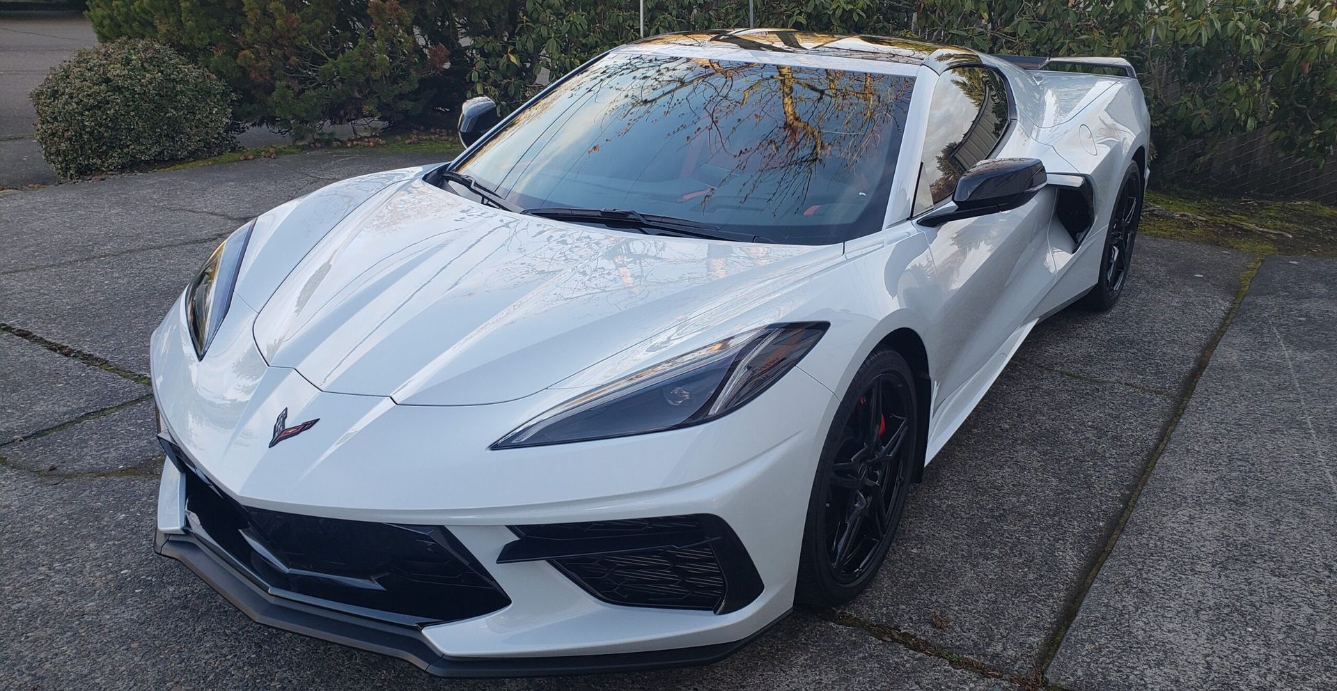 White Chevrolet Corvette sports car parked on a concrete driveway, front three-quarter view.