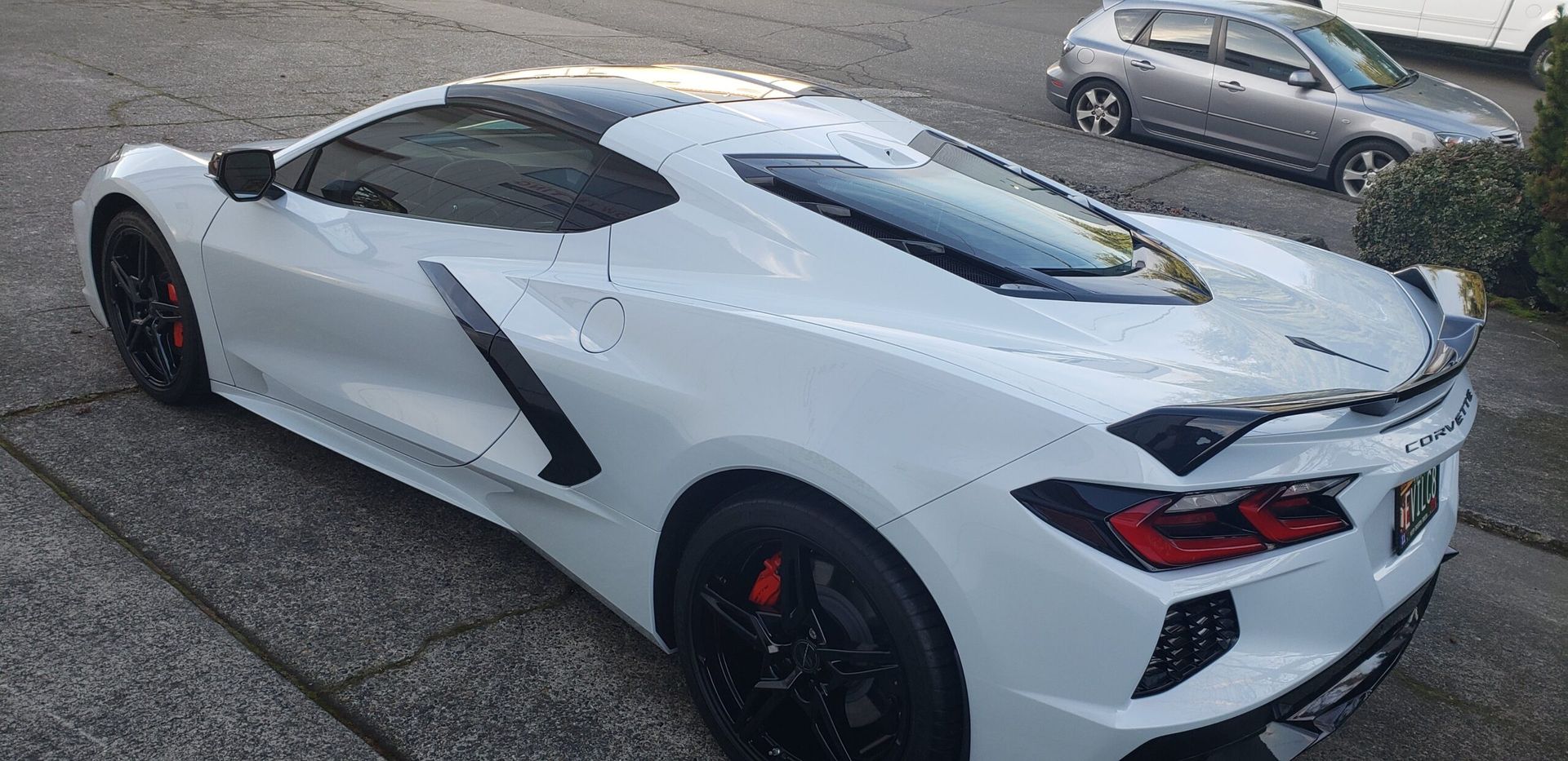 White sports car parked on a driveway, viewed from the rear side angle.