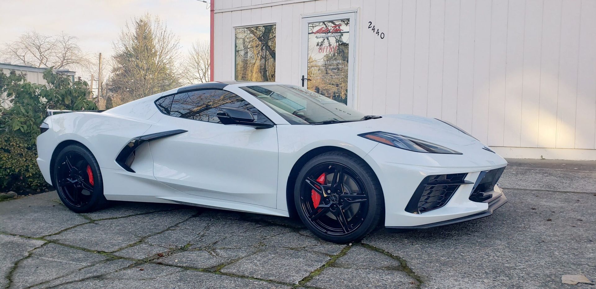 White sports car with red brake calipers parked on a driveway beside a building