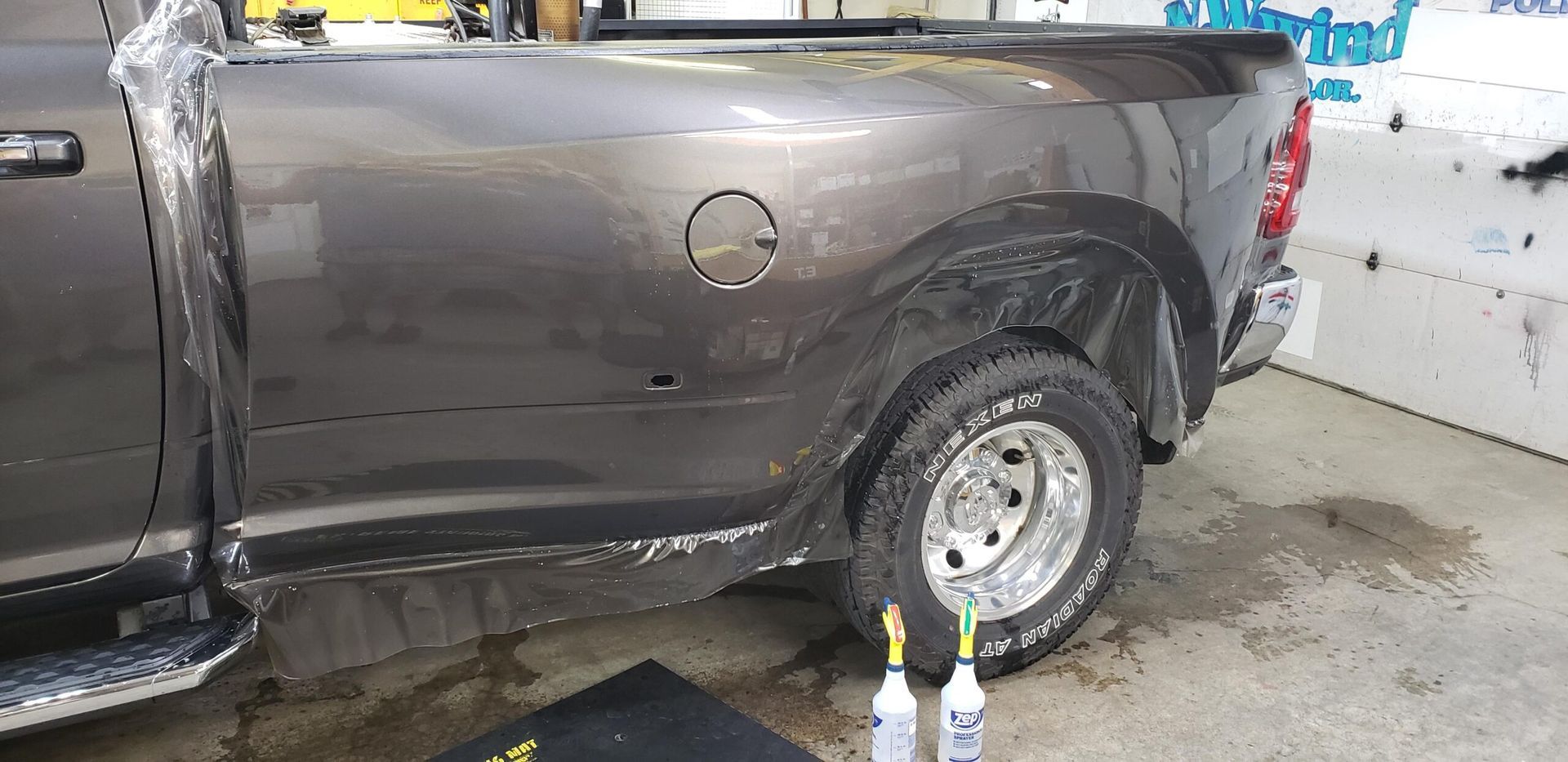 Gray pickup truck with a dented rear side panel, parked beside a wall in a wash bay