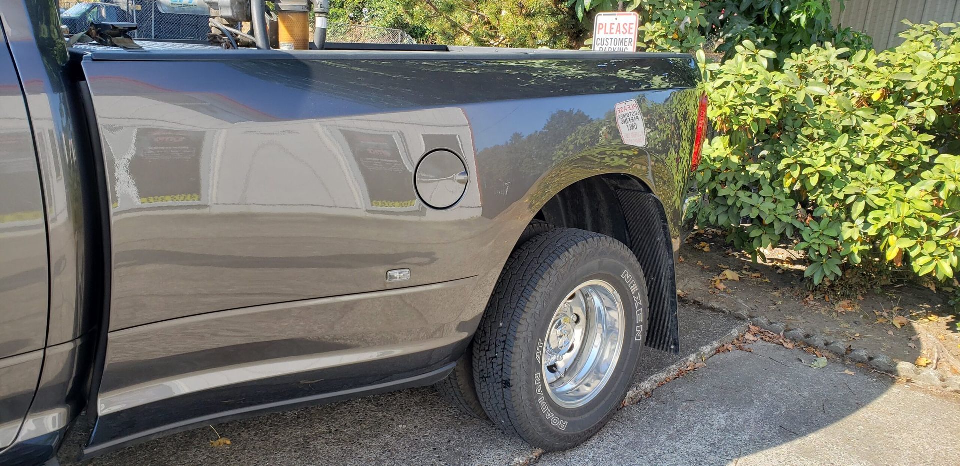 Gray pickup truck parked beside green bushes on a driveway, showing the rear side and wheel.