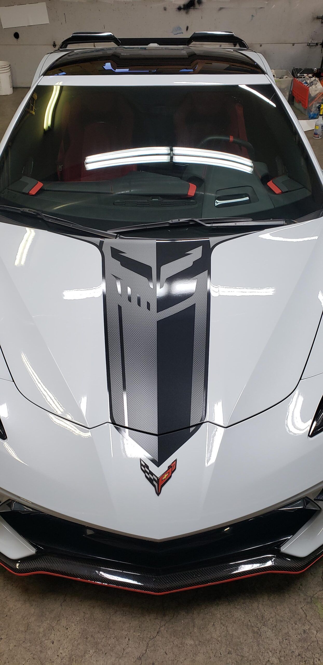 White Chevrolet Corvette with black racing stripe, front view, in a garage.