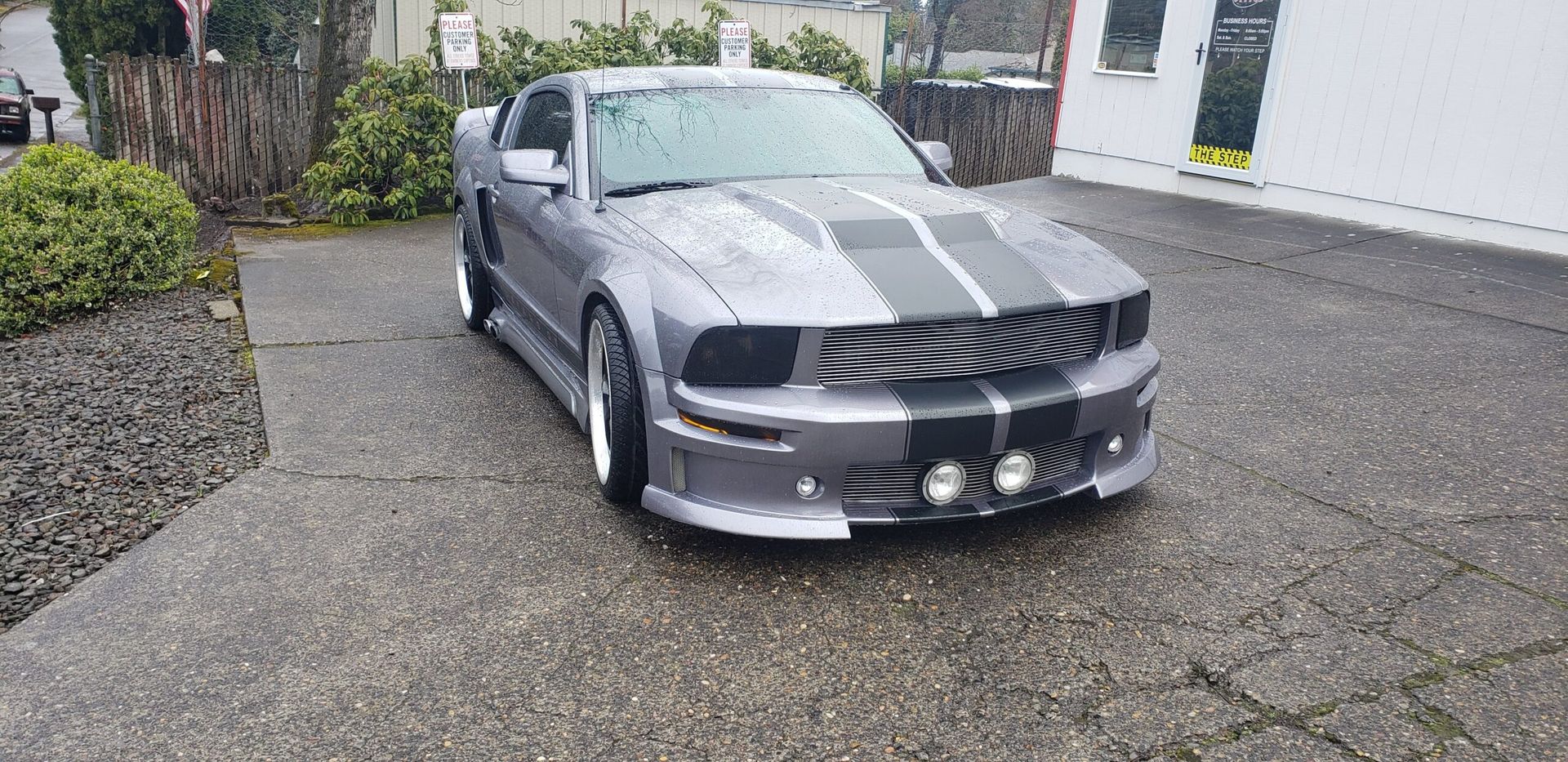 Gray sports car with black racing stripes parked in a driveway, front view