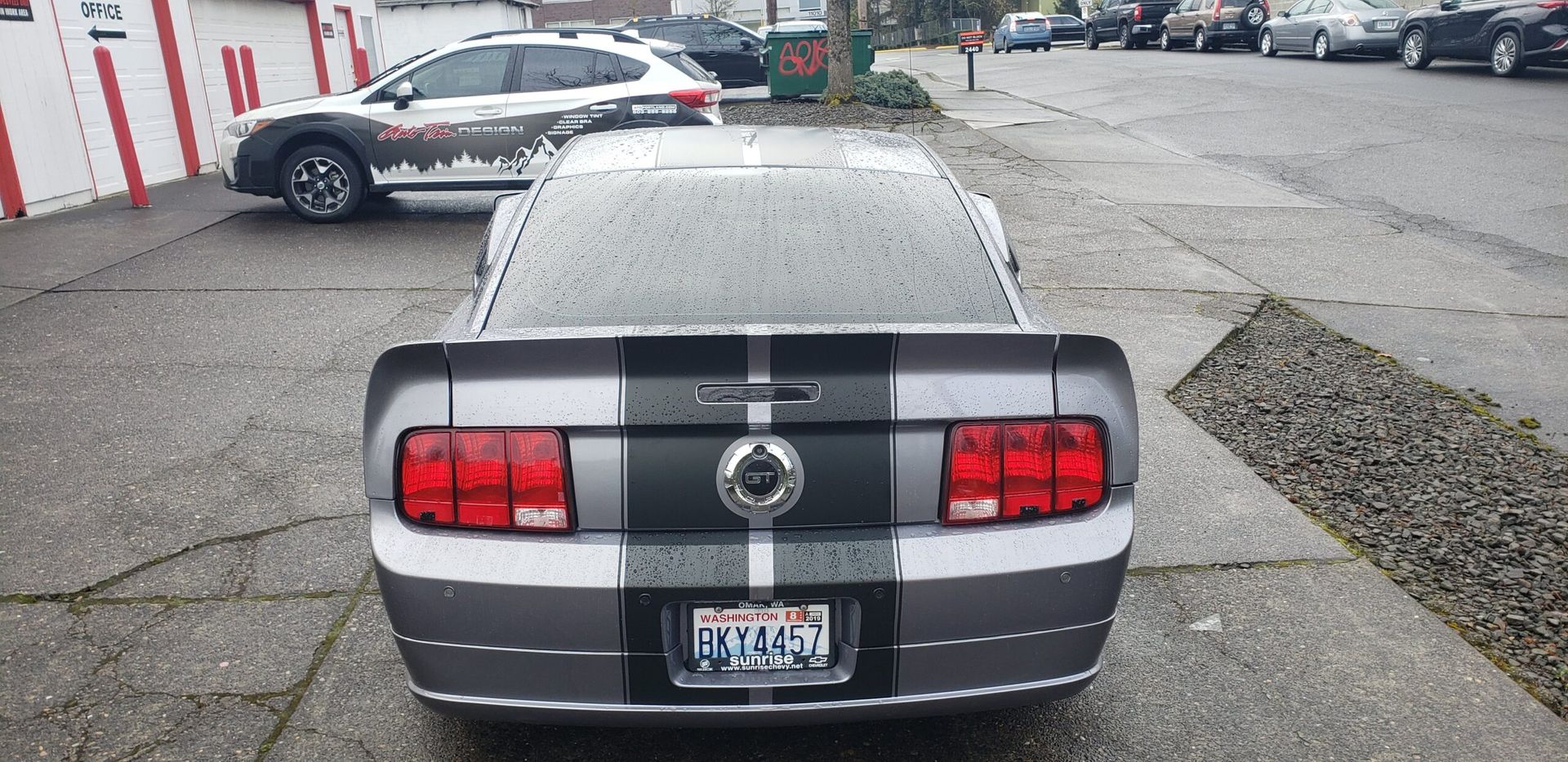 Gray sports car rear view in a parking lot with twin black racing stripes and snow on the roof