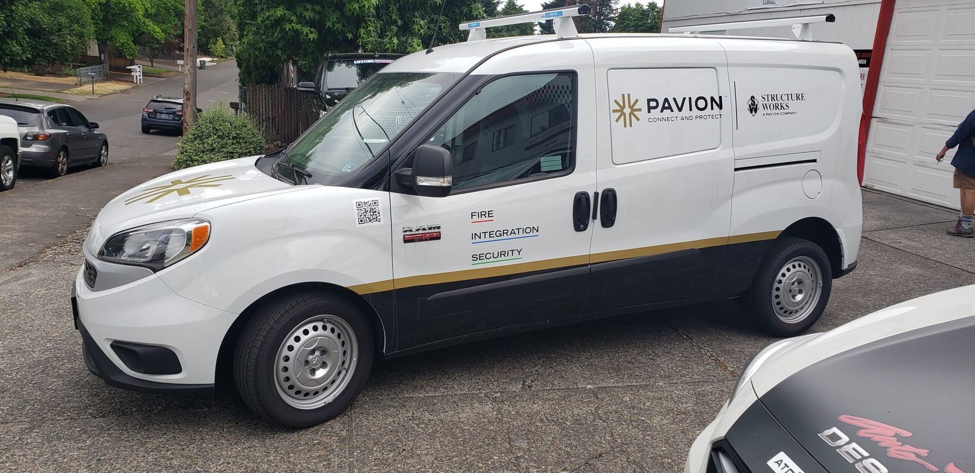 White cargo van with company logos parked on a street beside other cars and a sidewalk