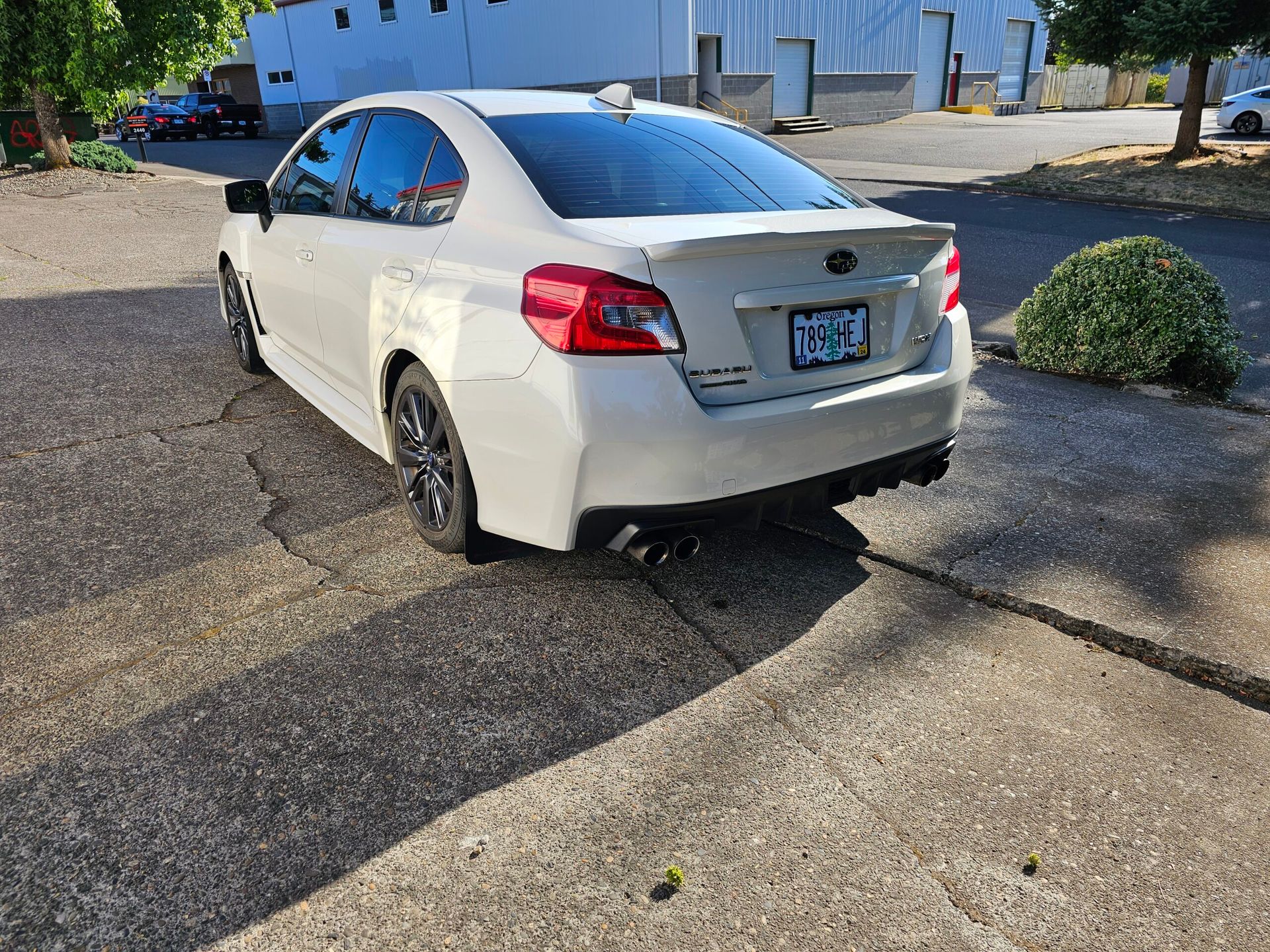 White sedan parked on a cracked driveway beside a building, rear view visible.