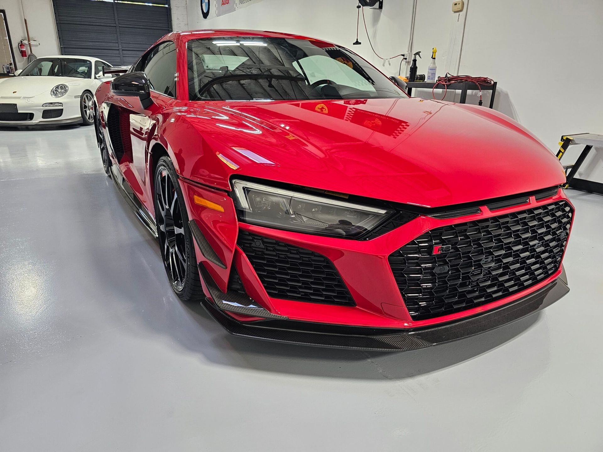 Red sports car in a garage, front view with black grille and trim, bright overhead lighting