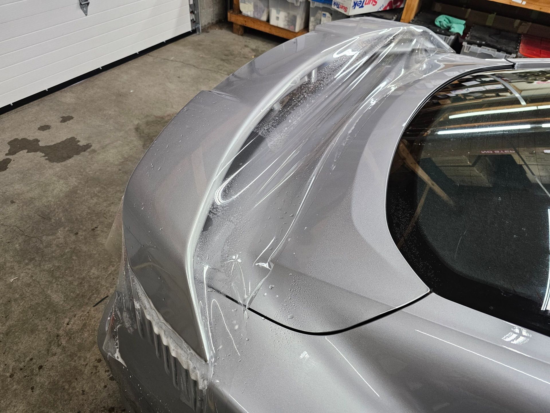 Silver car rear quarter panel wrapped in clear protective film inside a garage