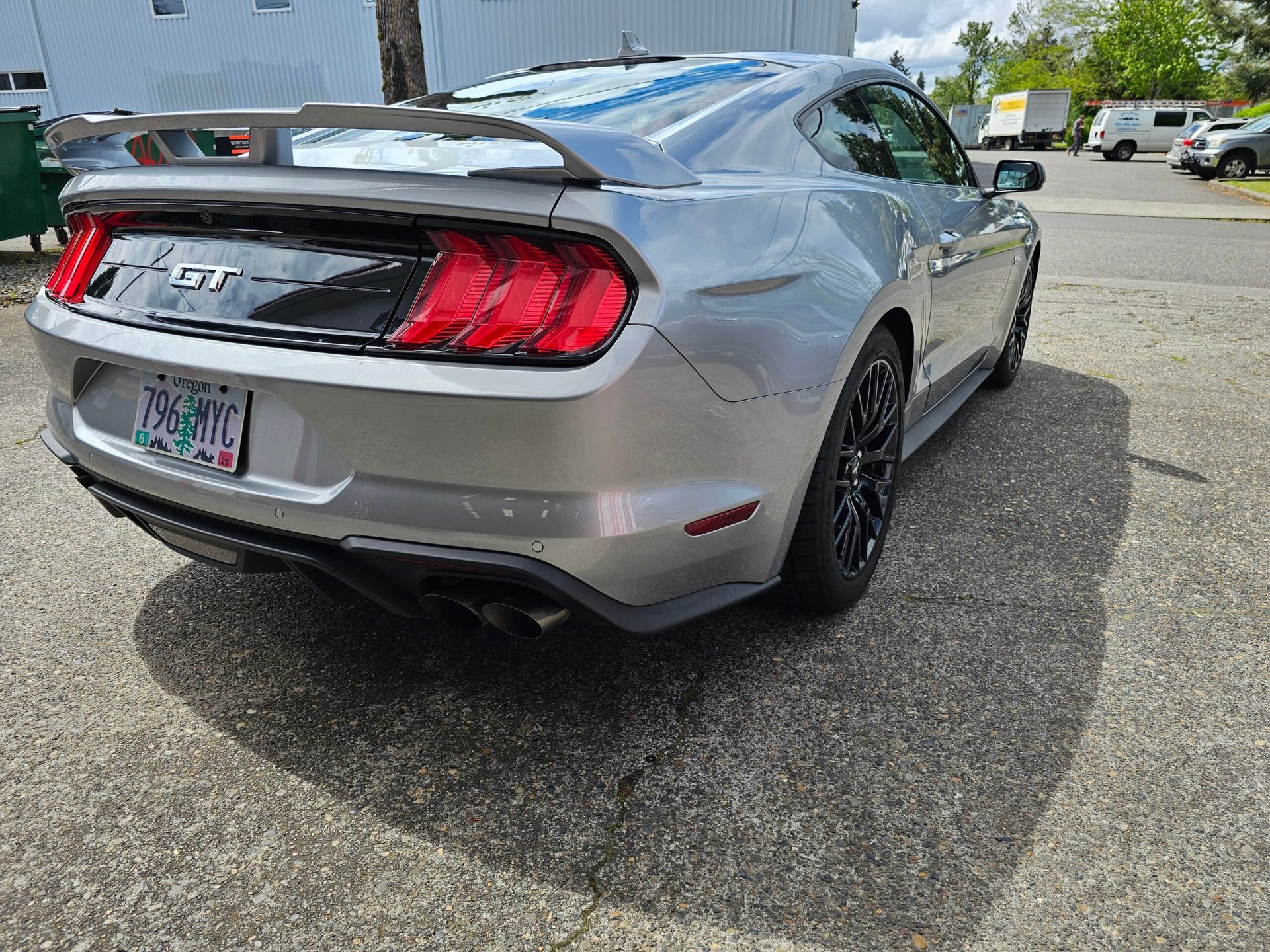 Gray Ford Mustang rear view in a parking lot, with black wheels and a rear spoiler.