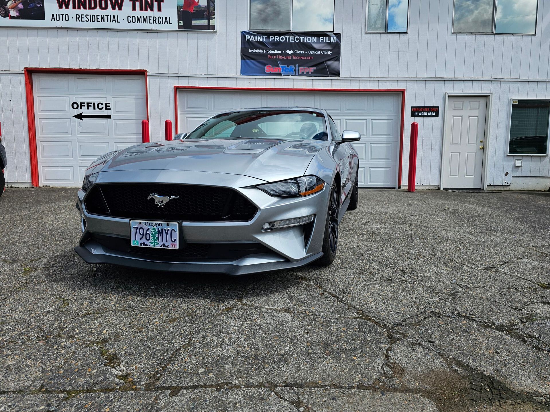 Silver Ford Mustang parked outside a garage with white doors and red trim