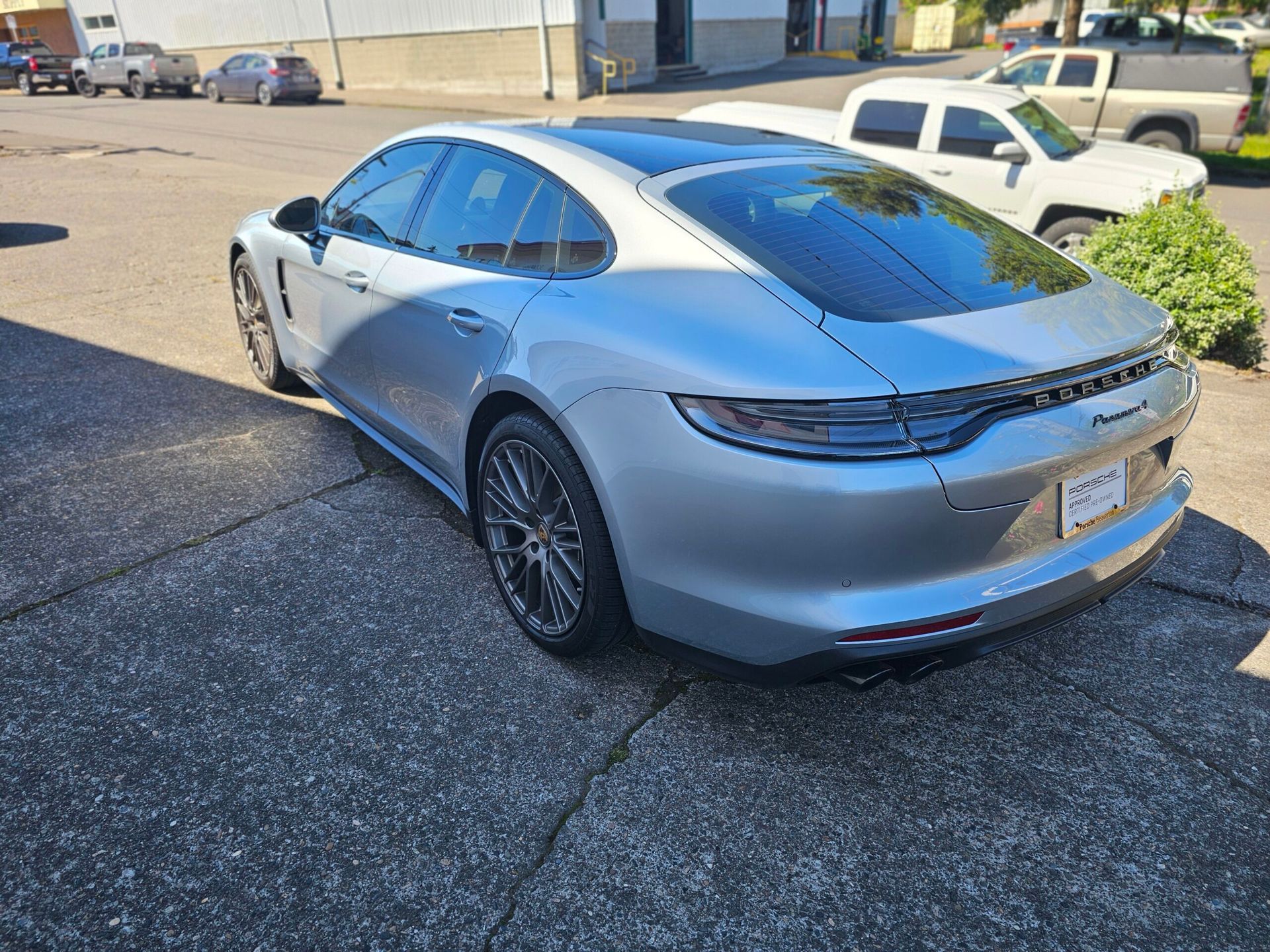 Silver sedan parked in a lot, rear three-quarter view under bright sunlight.