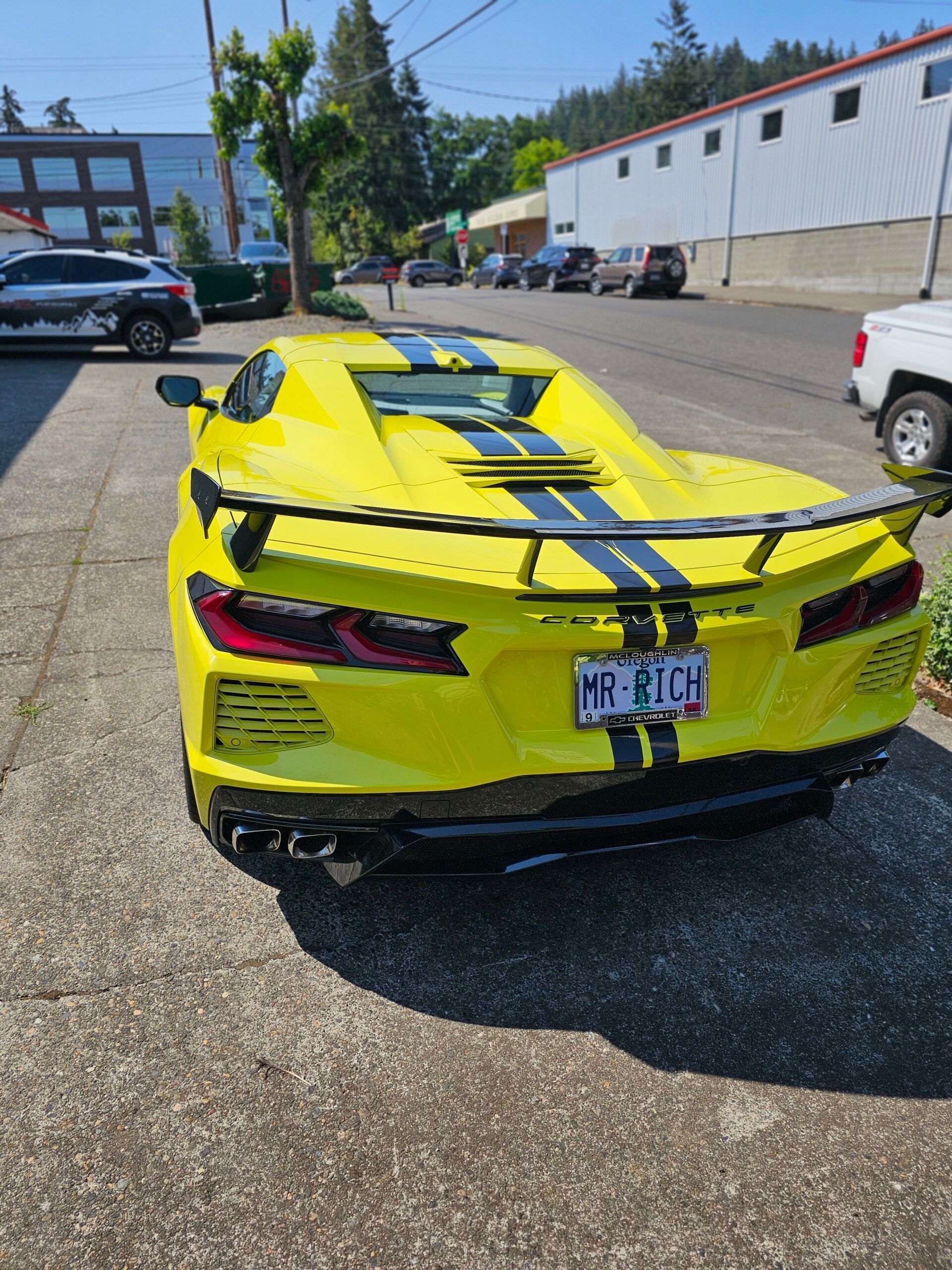Yellow sports car with black racing stripes parked in a lot, rear view