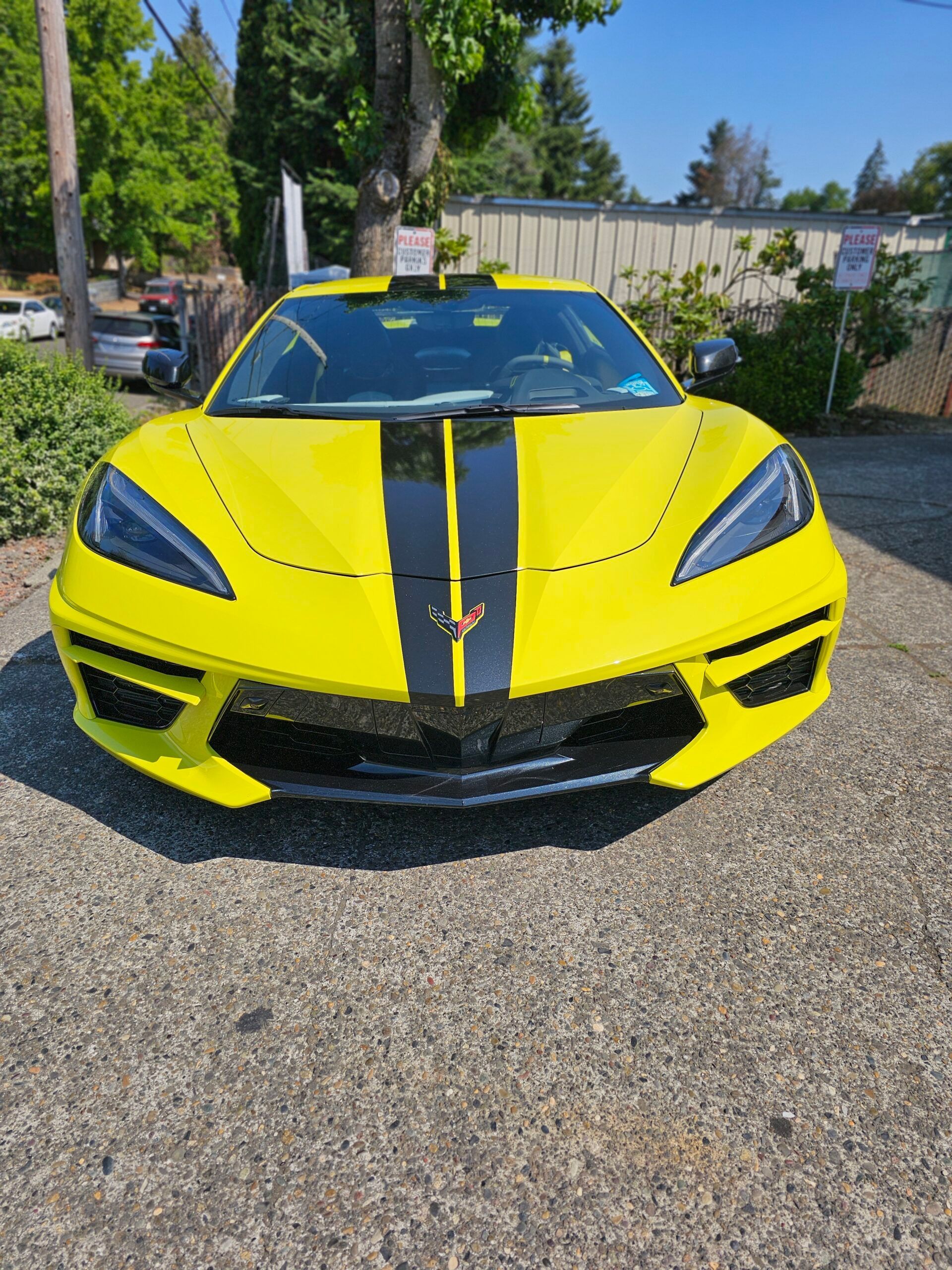 Bright yellow sports car with black racing stripes parked outdoors on a driveway