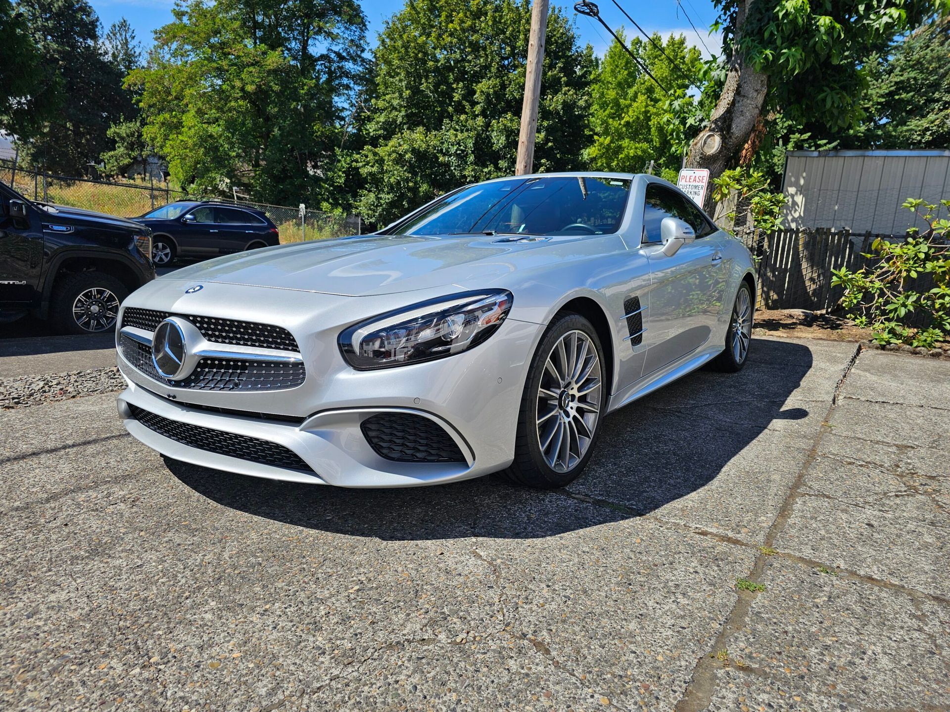 Silver Mercedes coupe parked on a driveway in bright sunlight, with trees and a house in the background