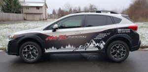 Black SUV with white mountain graphics parked on a wet road in a suburban neighborhood