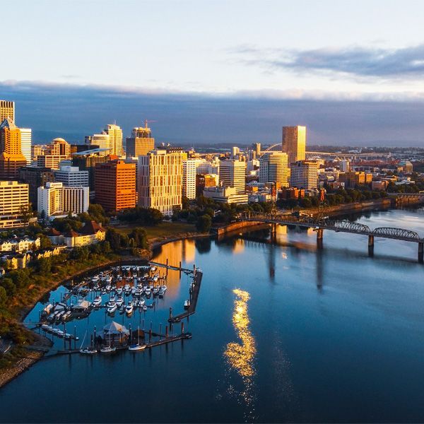 Sunlit city skyline along a river with a marina and bridge at sunset