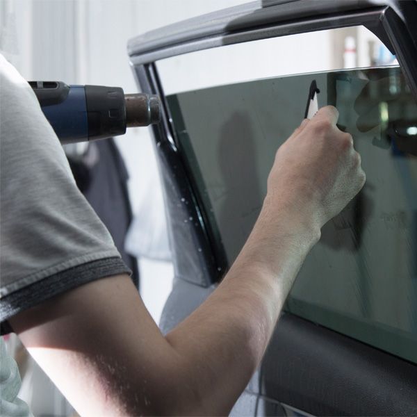 Person using a drill to work on a car window in a garage