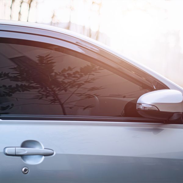 Silver car side view with tinted window and door handle in bright sunlight