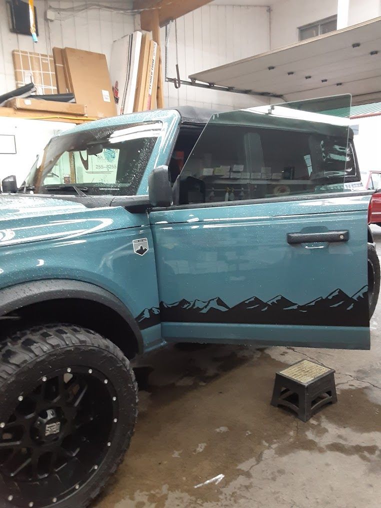 Turquoise off-road SUV with open driver door in a garage, showing black wheels and a lifted suspension.