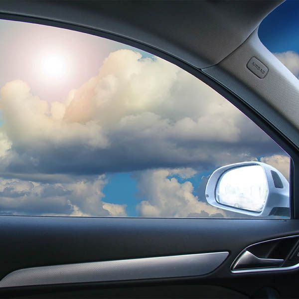 Car interior view of bright clouds and sun outside the window, with side mirror and door visible