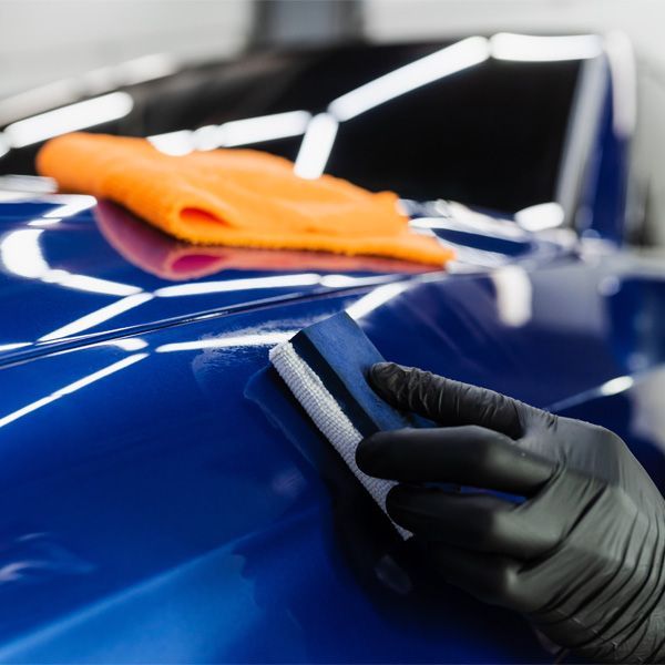 Black-gloved hand polishing a blue car with a cloth in a detailing shop