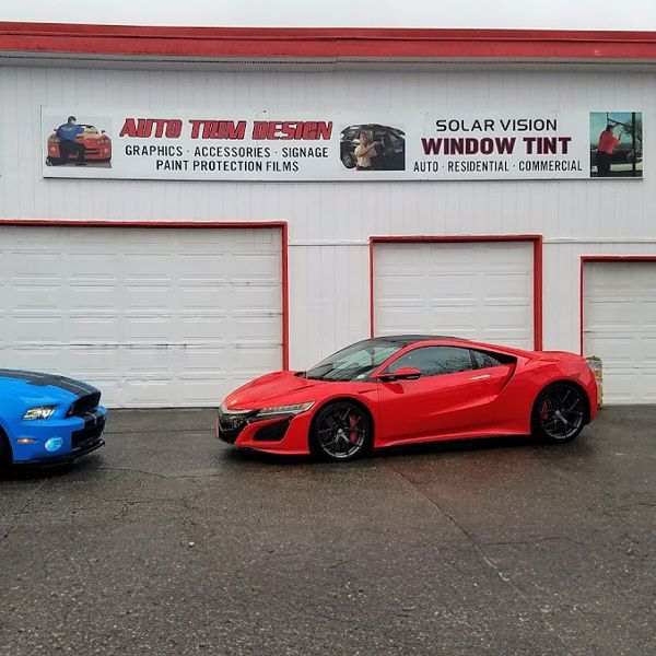 Two sports cars parked outside an auto customization shop, with a red coupe centered in front of garage doors.