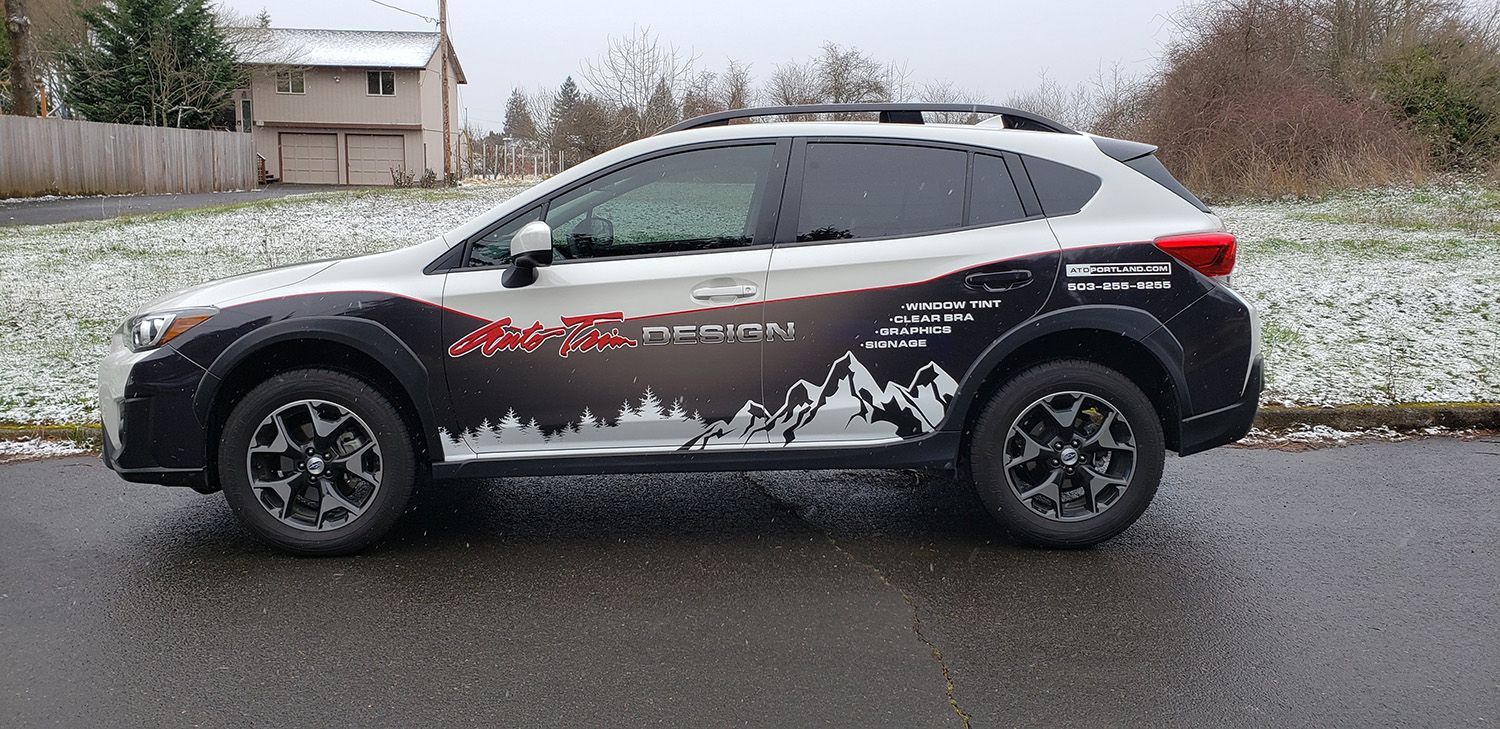 Black SUV with snow-dusted roof and racing graphics parked on a wet street