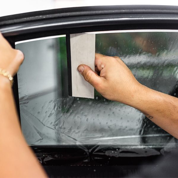 Hands using a squeegee to clear water from a car window in the rain