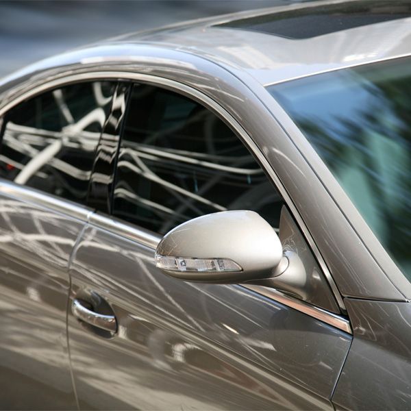 Close-up of a silver car door and side mirror with tinted window reflections